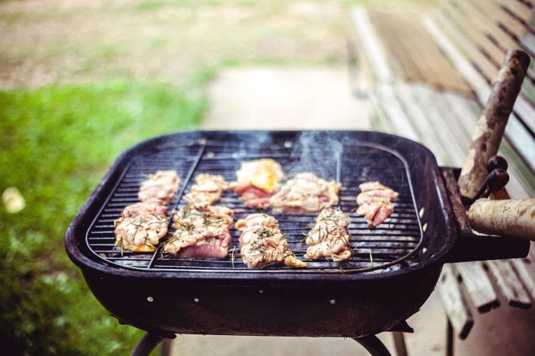 Beef and chicken sizzling on a charcoal grill during a sunny outdoor cookout