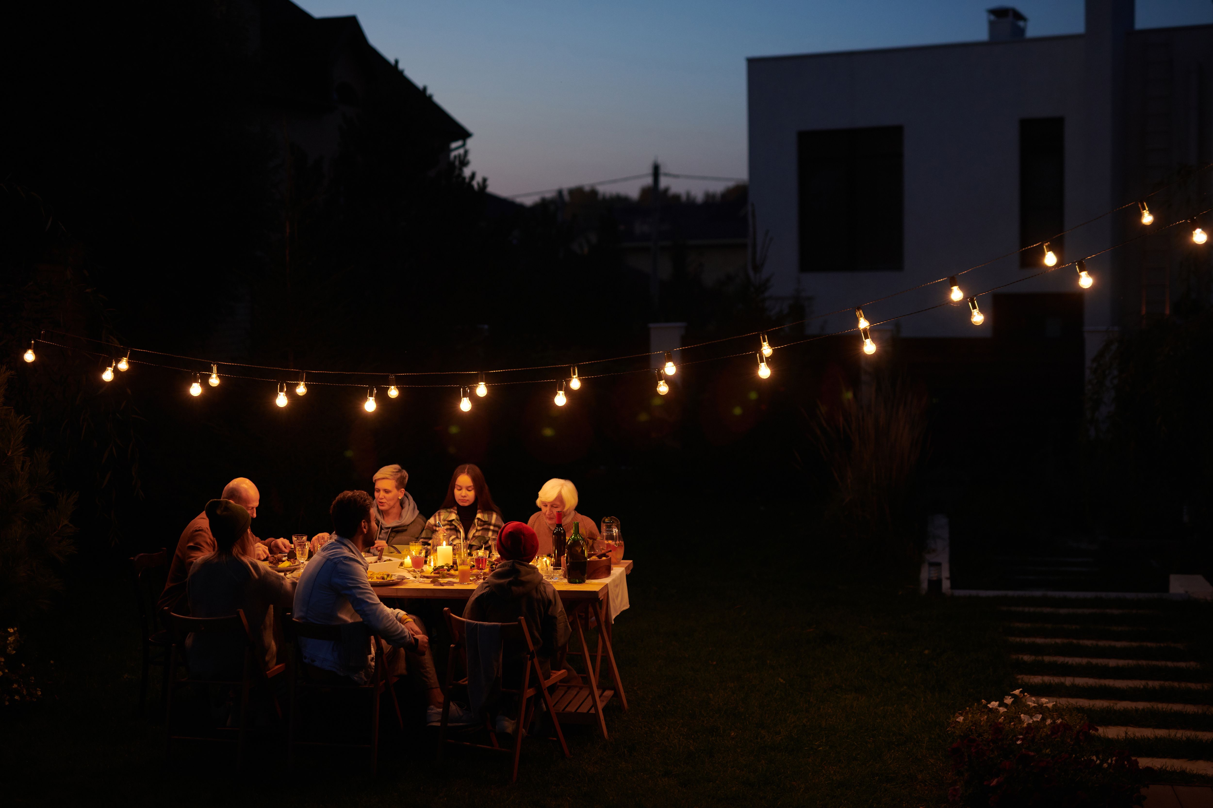 A family enjoying an evening meal outdoors under decorative string lights